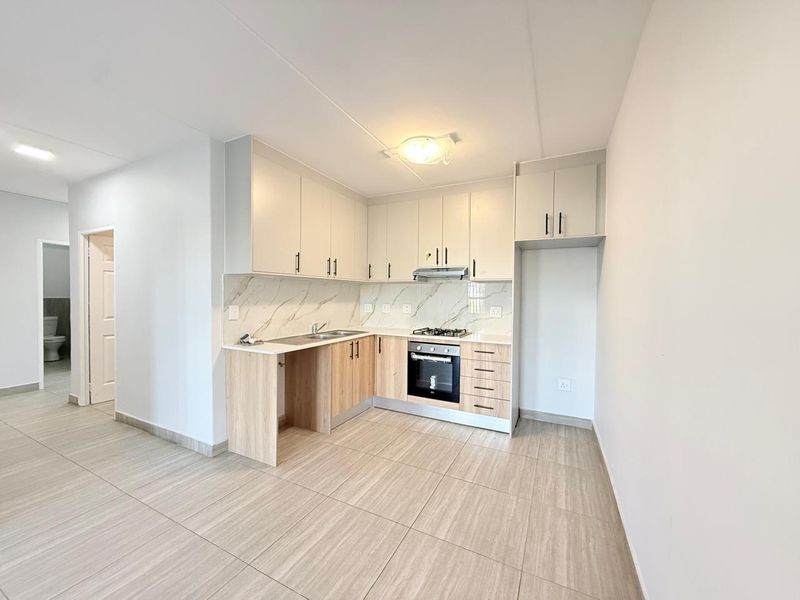 Modern kitchen featuring light wood-tone cabinetry, marble-effect backsplash, built-in oven, gas hob, and neutral floor tiles in an open-plan layout.