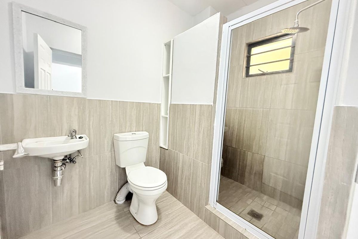 A modern bathroom featuring neutral floor-to-ceiling tiling, a glass-enclosed shower with a rain shower head, a wall-mounted basin, and a toilet.