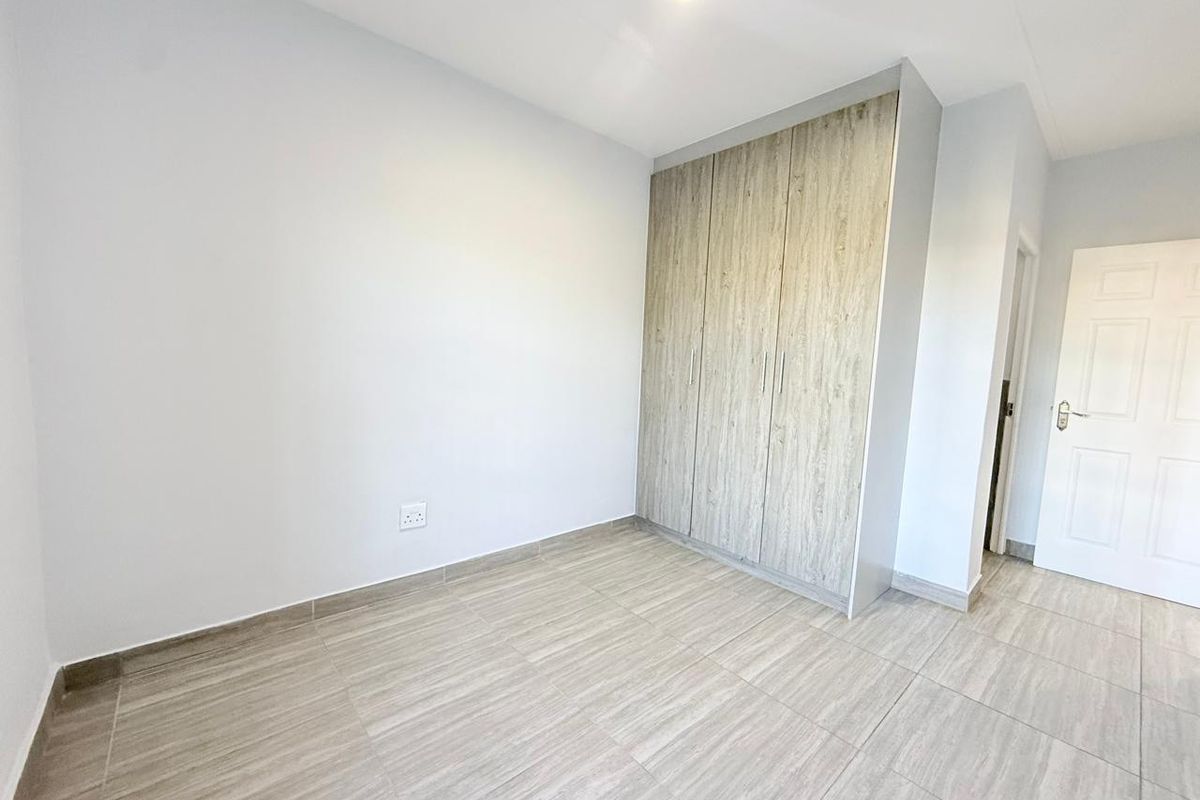 A clean, empty bedroom featuring modern wood-look tiled flooring and built-in cupboards with a neutral finish.