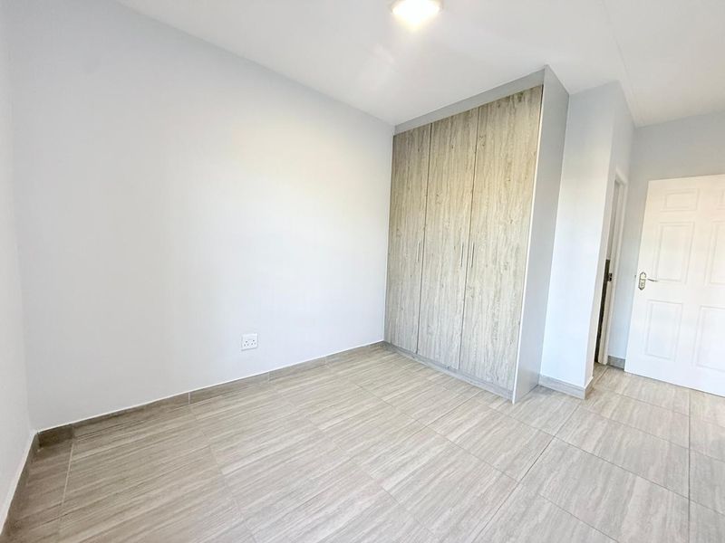 A clean, empty bedroom featuring modern wood-look tiled flooring and built-in cupboards with a neutral finish.