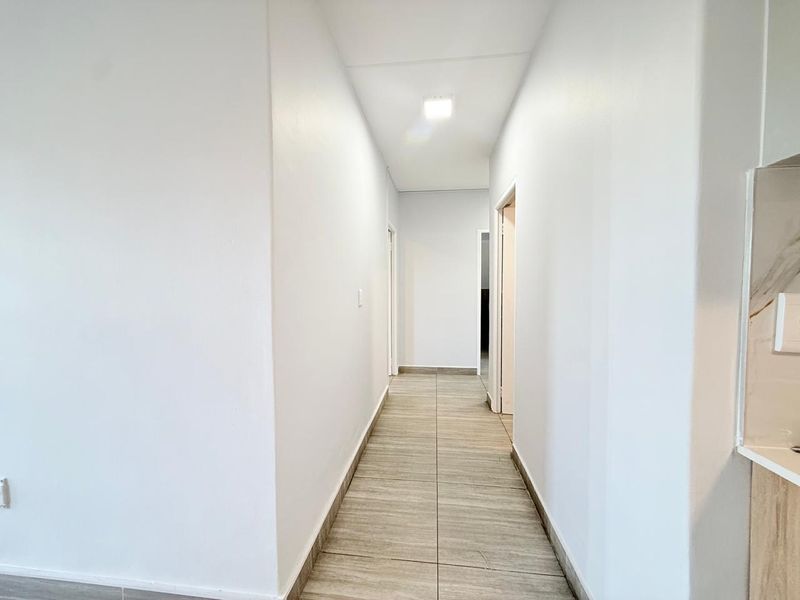 A clean, neutral hallway featuring modern tiled flooring and recessed ceiling lighting, providing a bright and seamless transition between rooms.