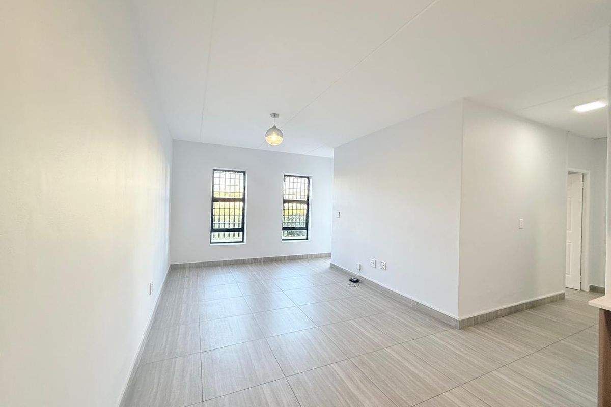 A bright, empty living area featuring modern wood-look floor tiles, neutral walls, and security-fitted windows, offering a clean and versatile space.