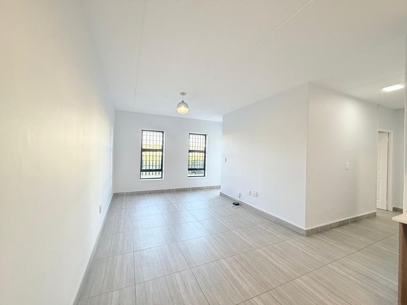A bright, empty living area featuring modern wood-look floor tiles, neutral walls, and security-fitted windows, offering a clean and versatile space.