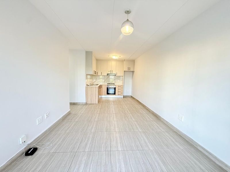 An open-plan living and kitchen area featuring modern light-wood cabinetry, built-in oven and hob, and neutral tiled flooring throughout.