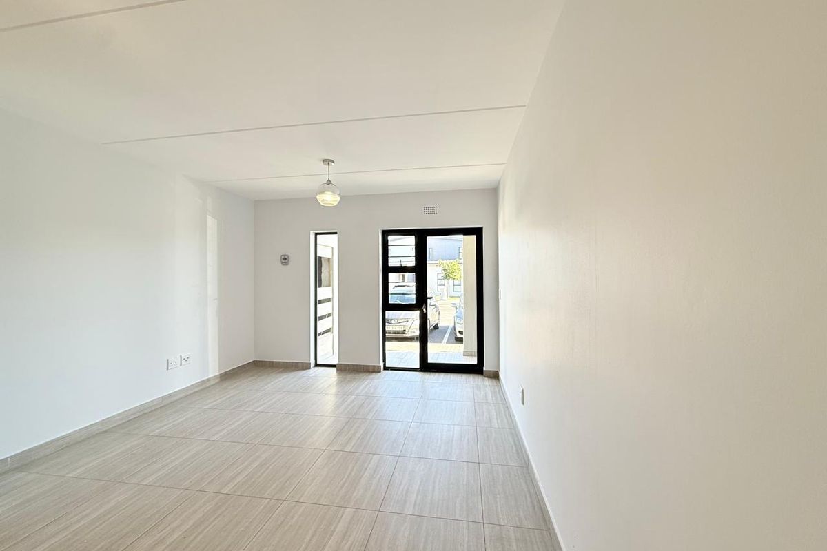 A bright, empty living area featuring neutral tiled flooring, a modern pendant light, and a glass-paneled door providing access to the exterior.