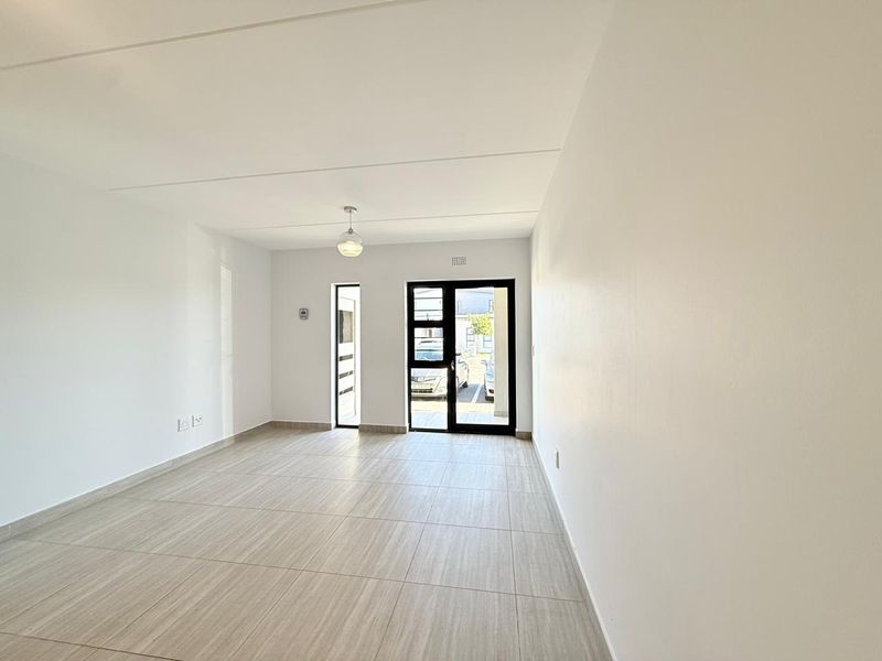 A bright, empty living area featuring neutral tiled flooring, a modern pendant light, and a glass-paneled door providing access to the exterior.