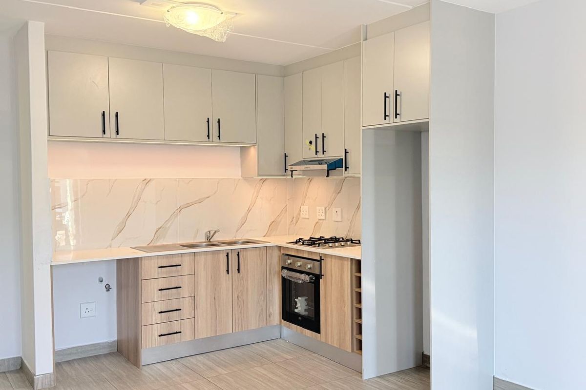 Modern kitchen featuring light wood-tone cabinetry, marble-look splashback, built-in oven, gas hob, and dedicated space for a refrigerator.