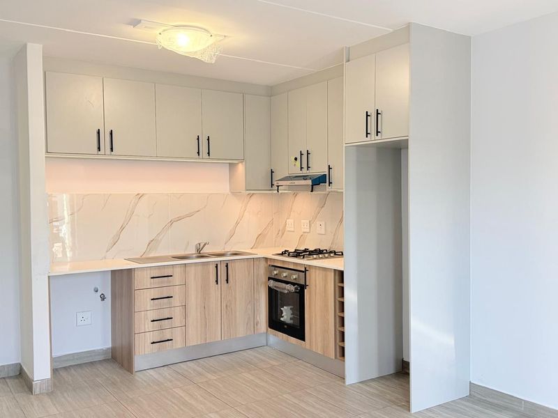 Modern kitchen featuring light wood-tone cabinetry, marble-look splashback, built-in oven, gas hob, and dedicated space for a refrigerator.