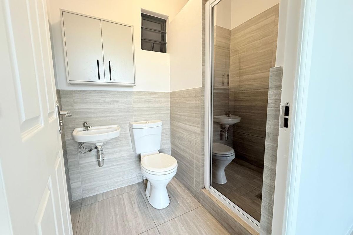 A clean, modern bathroom featuring a wall-mounted basin, toilet, and a glass-enclosed shower with neutral-toned wall and floor tiles.