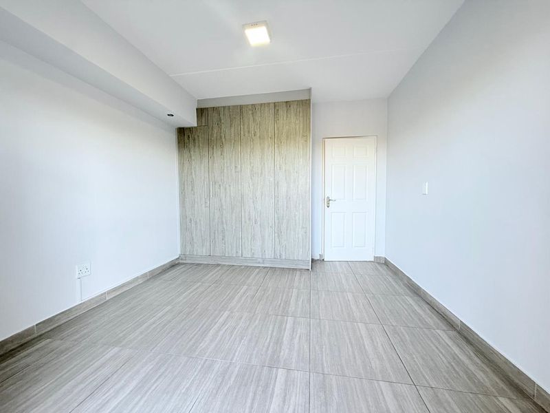 A bright, empty bedroom featuring modern wood-look tiled flooring and built-in cupboards, offering a clean and neutral space ready for personalization.