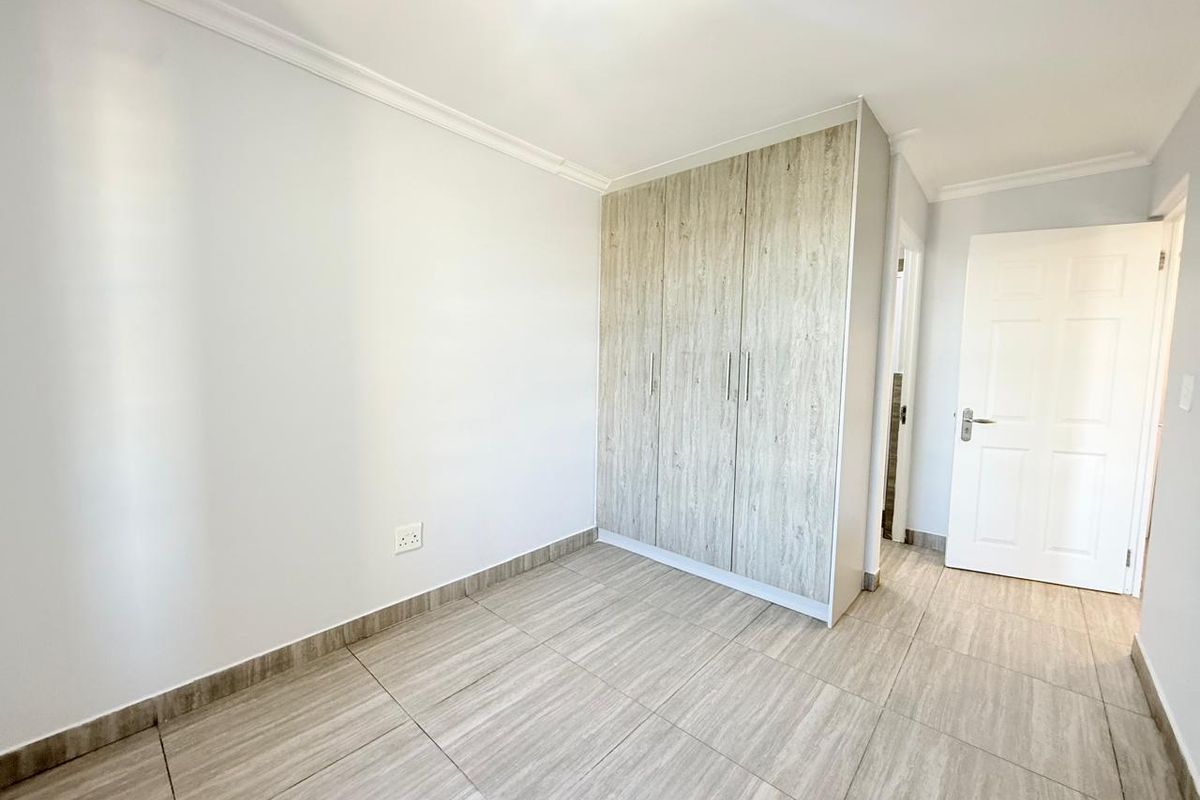 A bright, empty bedroom featuring modern wood-look tiled flooring and built-in cupboards with a light wood finish.