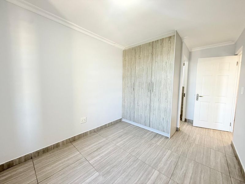 A bright, empty bedroom featuring modern wood-look tiled flooring and built-in cupboards with a light wood finish.