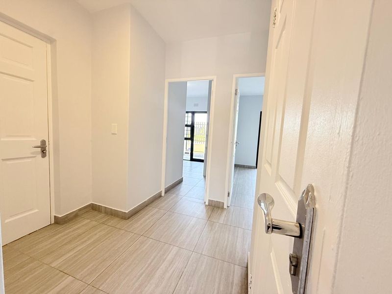 A clean, neutral hallway featuring modern tiled flooring and multiple internal doorways leading to adjacent rooms within the apartment.