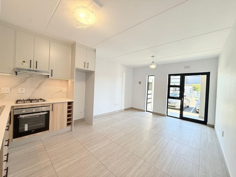Modern open-plan kitchen and living area featuring contemporary cabinetry, integrated appliances, neutral tile flooring, and direct access to the exterior.