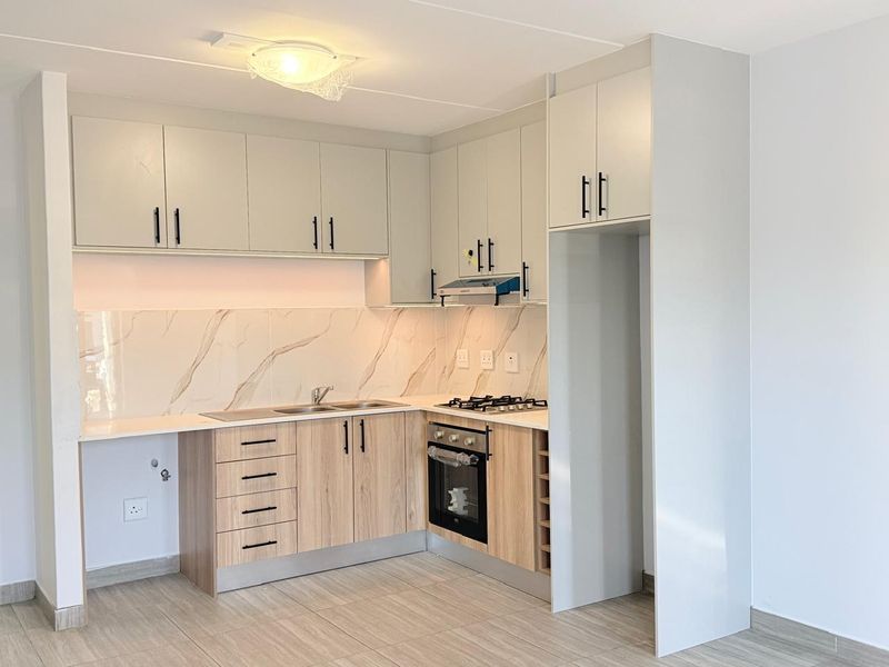 Modern, well-maintained kitchen featuring light wood-finish cabinetry, marble-look splashback, gas hob, built-in oven, and dedicated space for a refrigerator.