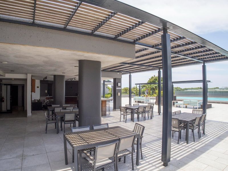 Spacious covered patio area featuring a modern pergola, tiled flooring, and a built-in bar, ideal for outdoor entertaining and relaxation.