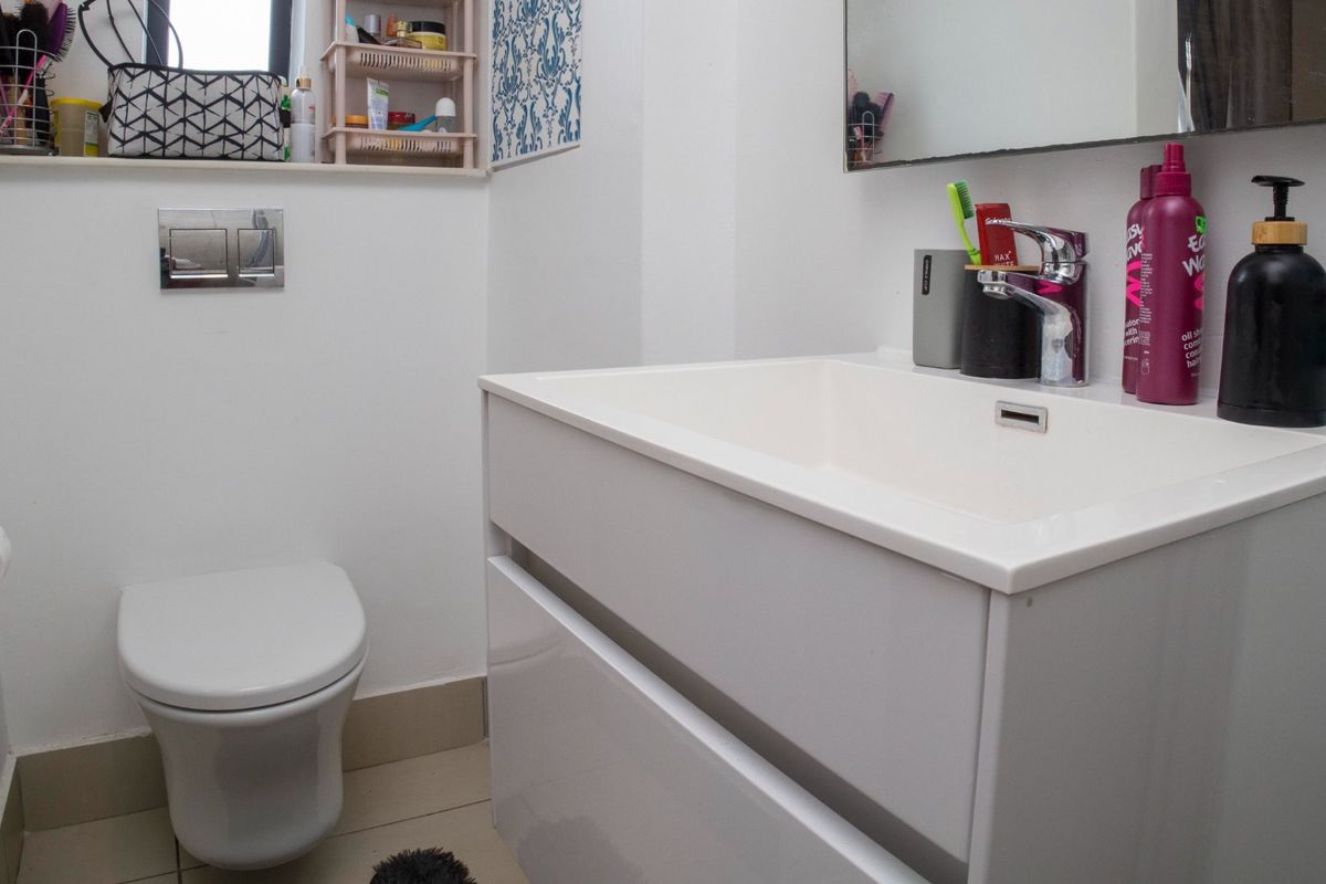 A modern bathroom featuring a wall-mounted toilet, a sleek vanity cabinet with an integrated basin, and a wall-mounted mirror.