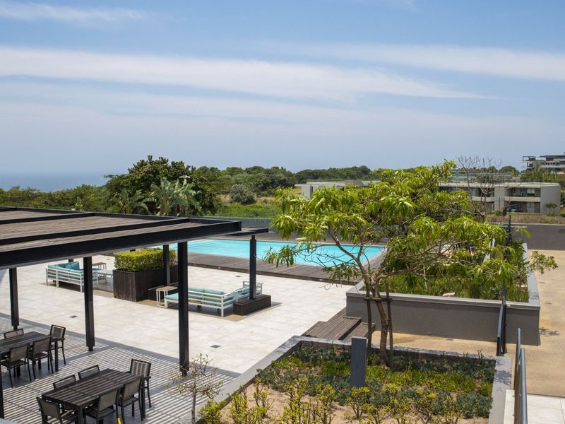 A well-maintained outdoor pool area featuring a timber pergola, tiled patio, and glass balustrades with scenic views.