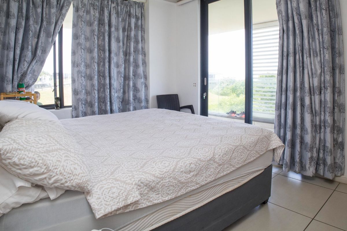 A bright bedroom featuring tiled flooring and a large sliding glass door that provides access to an outdoor balcony area.