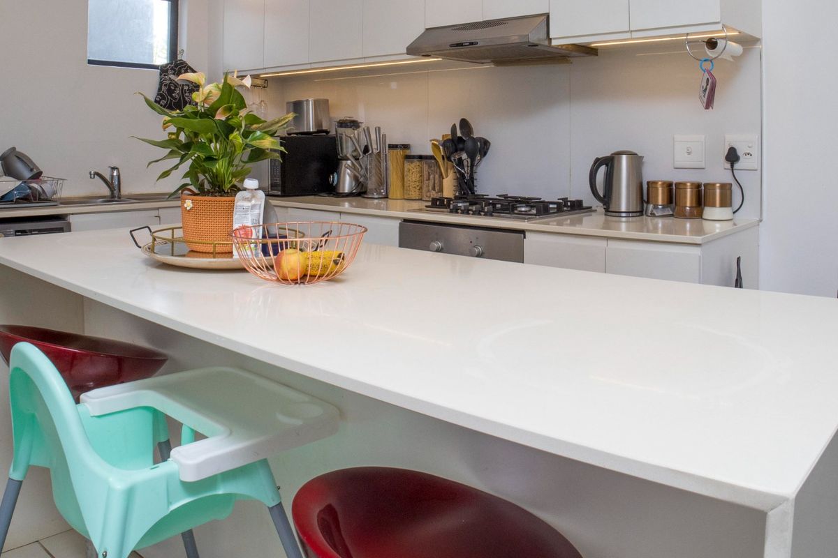 Modern kitchen featuring a large white quartz breakfast island, gas hob, built-in oven, and sleek cabinetry with integrated under-cabinet lighting.