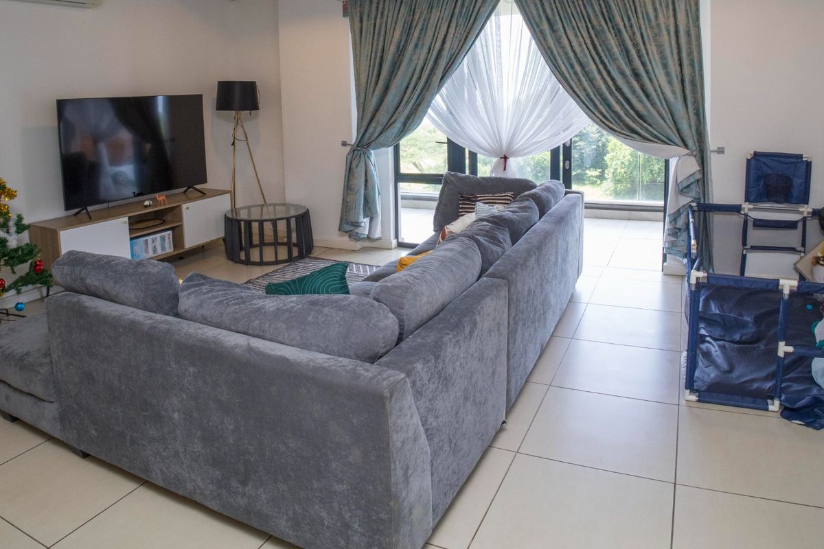 A comfortable living room featuring large format floor tiles, an air conditioning unit, and a sliding glass door providing access to the balcony.