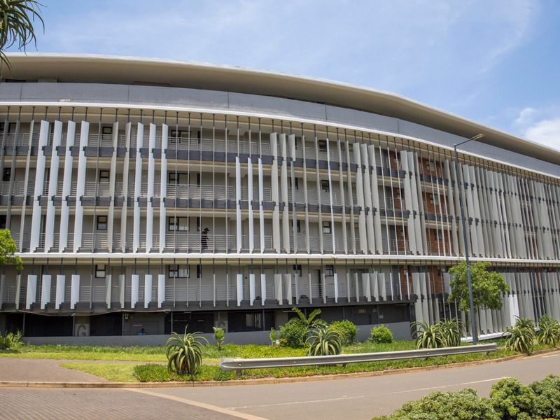 Modern apartment building exterior featuring a curved facade with vertical louvers and integrated balconies, set within a well-maintained landscaped environment.