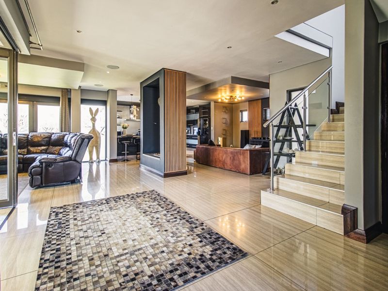 Spacious open-plan living area featuring polished tiled floors, a modern staircase with glass balustrades, and a central architectural feature pillar.