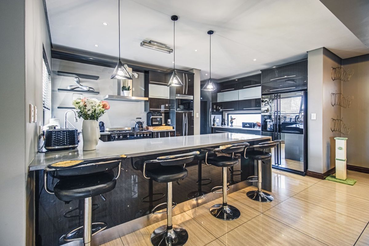 Modern kitchen featuring a large island with stone countertops, high-gloss cabinetry, integrated appliances, and stylish pendant lighting over the breakfast bar.