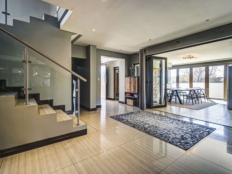 Spacious open-plan living area featuring a modern staircase with glass balustrades, large format floor tiles, and bi-fold doors leading to an outdoor space.