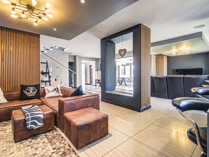 Spacious open-plan living area featuring modern slatted timber wall accents, polished tiled flooring, and a contemporary glass balustrade staircase.