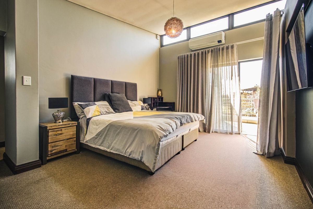 Spacious bedroom featuring high ceilings with clerestory windows, carpeted flooring, and direct access to an outdoor balcony through sliding glass doors.