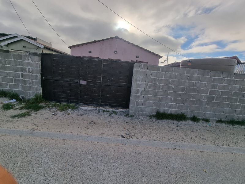 Front view of the property featuring a concrete block boundary wall, metal driveway gate, and a water storage tank.