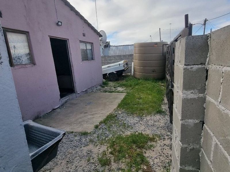 Rear exterior view of the property featuring a concrete patio, water storage tank, and boundary walling in a modest yard setting.