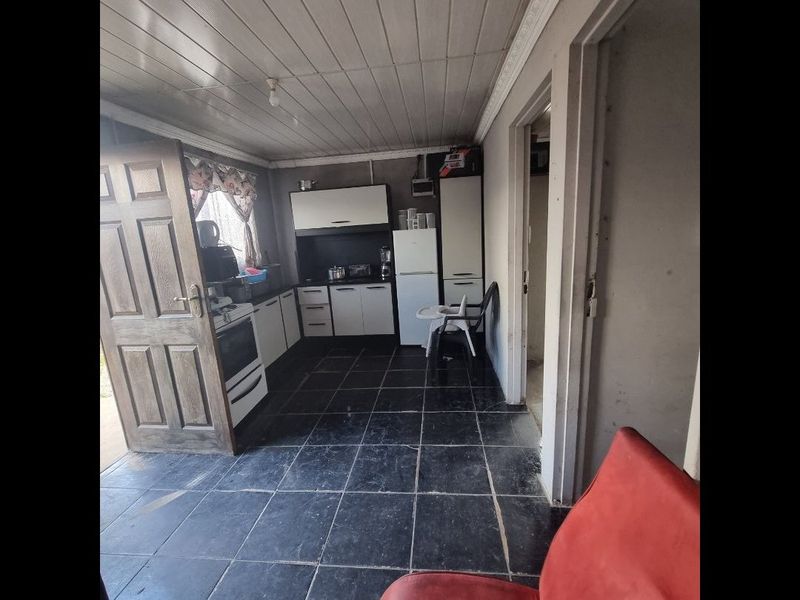 A functional kitchen space featuring built-in cabinetry, tiled flooring, and a panelled ceiling, requiring cosmetic updates to improve its overall condition and appeal.