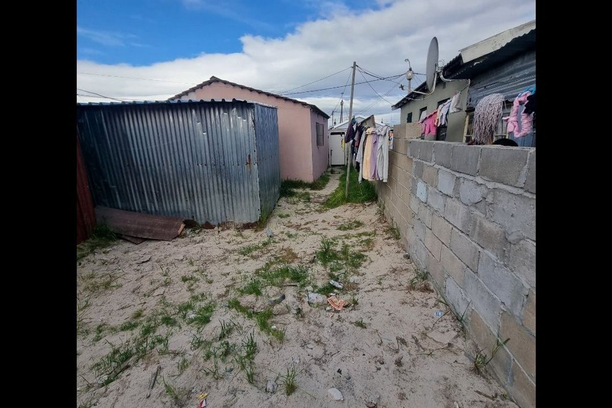 Rear exterior area featuring a corrugated metal shed, concrete block boundary wall, and unpaved sandy ground.