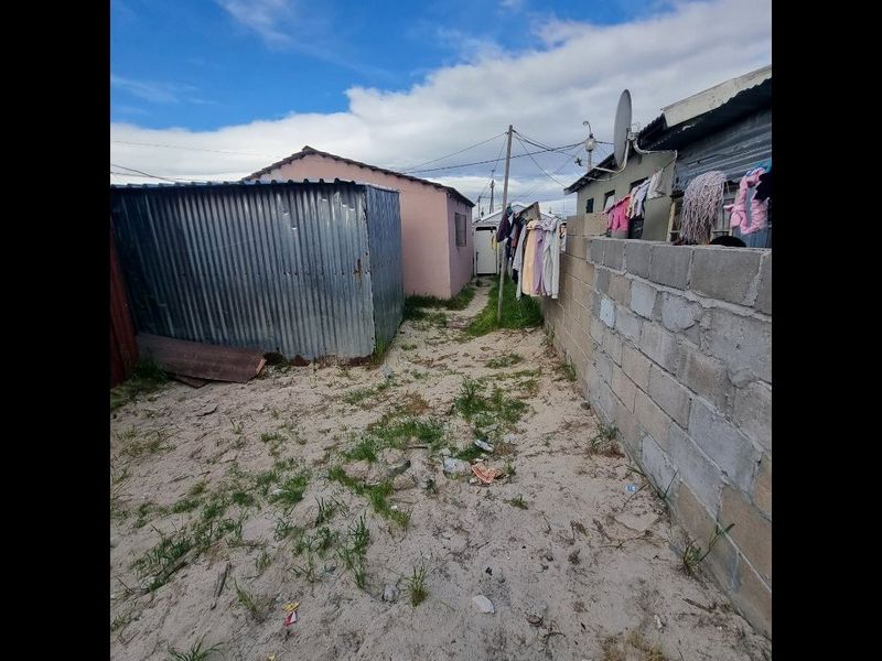 Rear exterior area featuring a corrugated metal shed, concrete block boundary wall, and unpaved sandy ground.