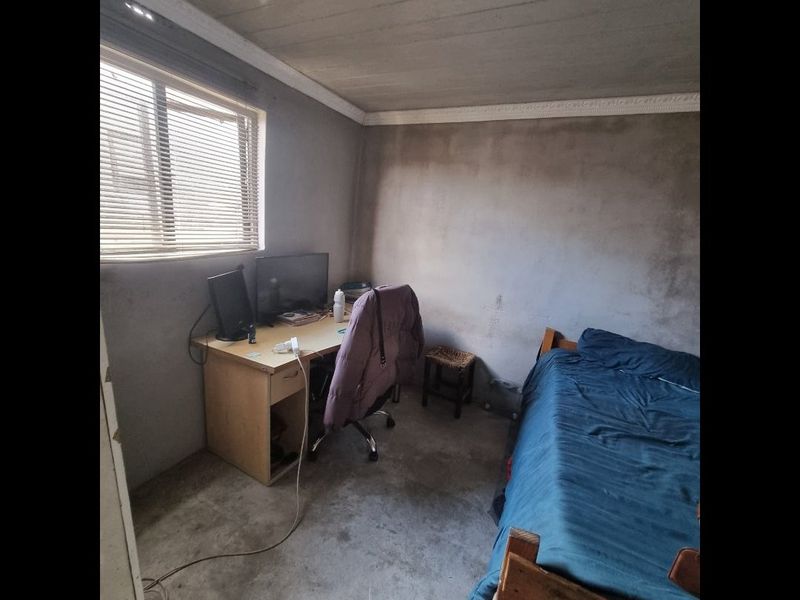 A bedroom featuring unfinished concrete walls and flooring, with a window fitted with venetian blinds and decorative ceiling cornice.