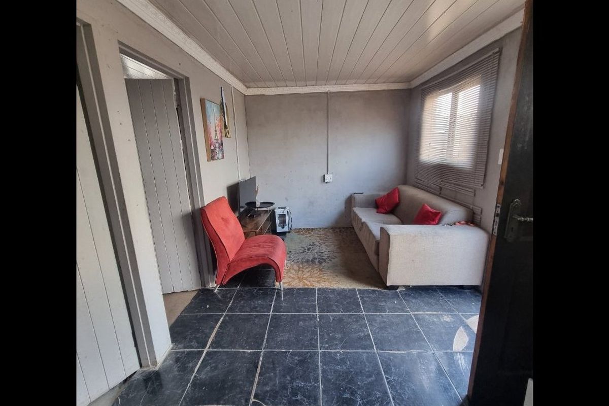 A living room featuring a timber-clad ceiling, tiled flooring, and exposed electrical conduit, offering a functional space with potential for cosmetic updates.