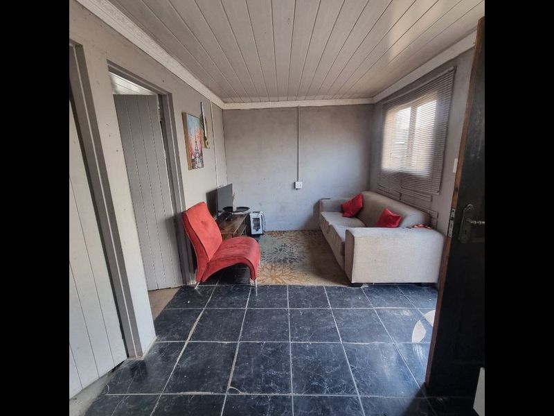 A living room featuring a timber-clad ceiling, tiled flooring, and exposed electrical conduit, offering a functional space with potential for cosmetic updates.