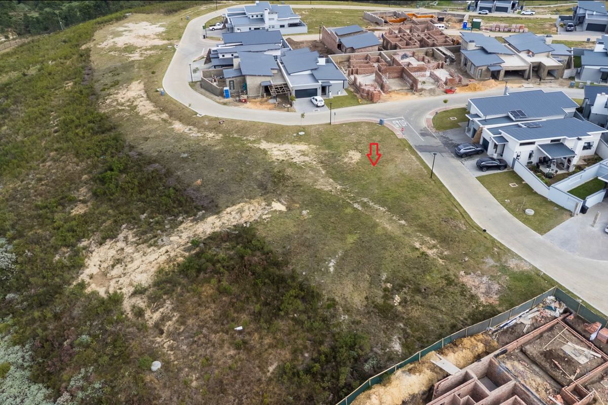 Aerial view of a vacant residential plot situated within a developed estate, featuring surrounding paved roads and nearby construction activity.