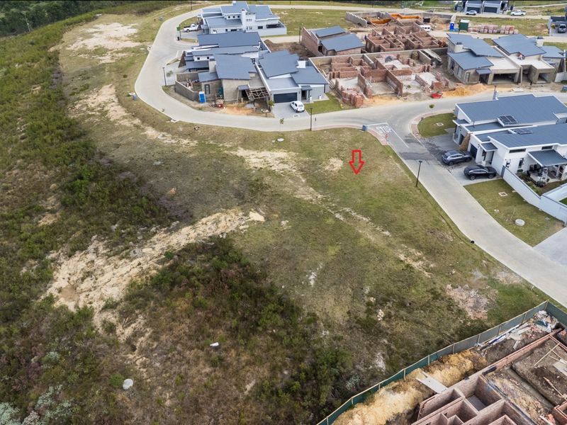 Aerial view of a vacant residential plot situated within a developed estate, featuring surrounding paved roads and nearby construction activity.
