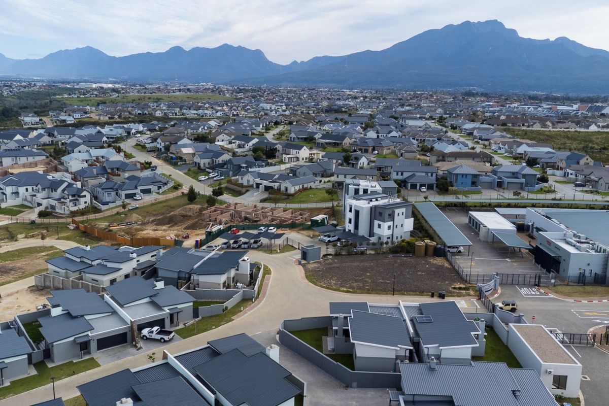 An aerial view of a modern residential estate featuring multiple homes, paved streets, and mountain views in the background.