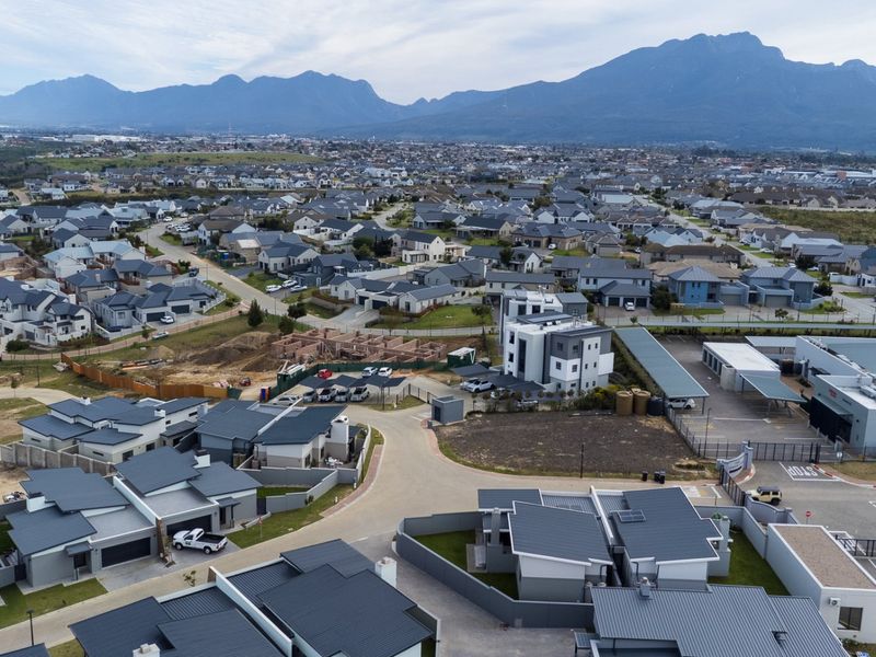 An aerial view of a modern residential estate featuring multiple homes, paved streets, and mountain views in the background.