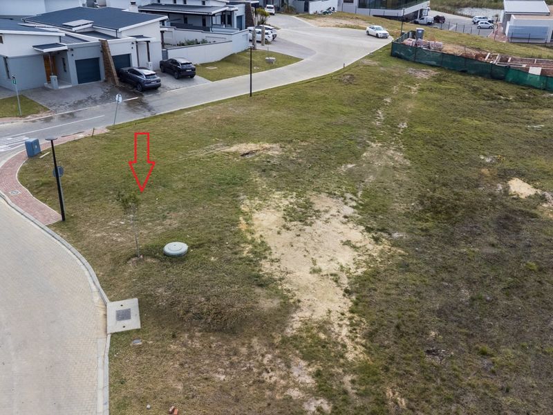 Aerial view of a vacant residential plot situated on a corner in a developed estate, featuring established road infrastructure and utility access points.