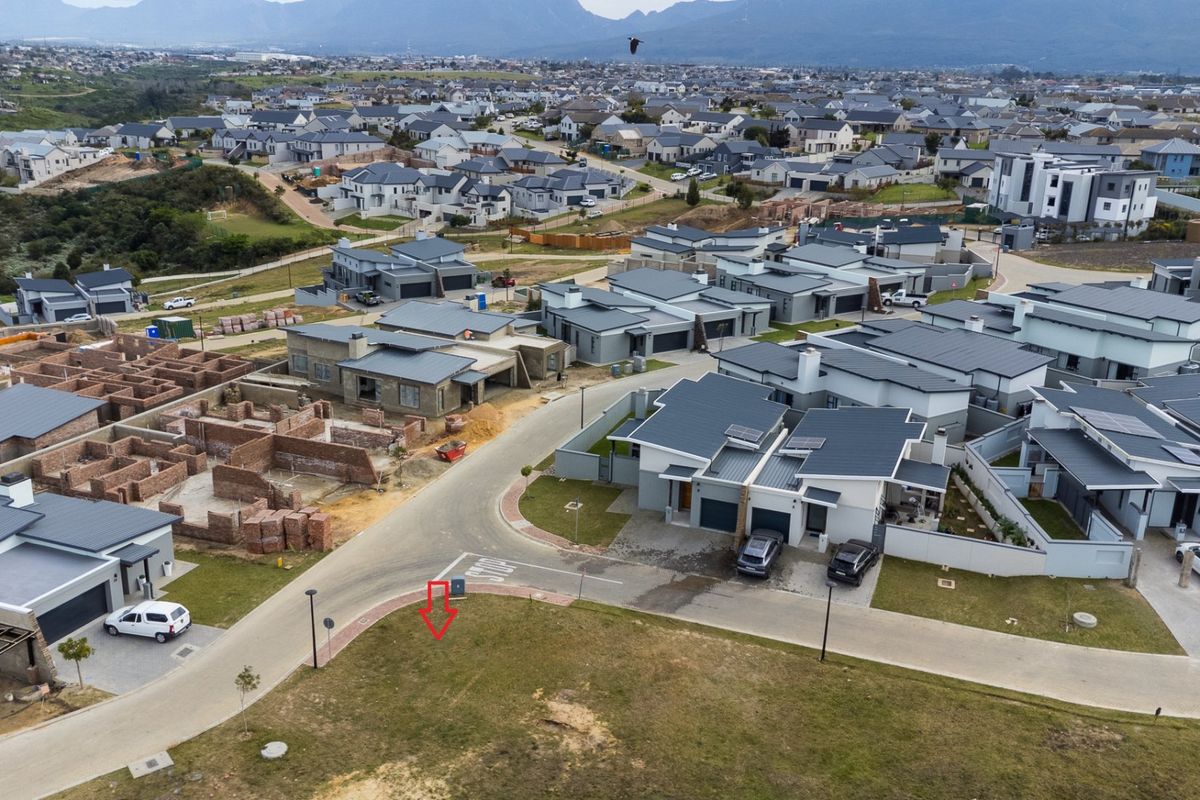 Aerial view of a vacant residential plot situated within a modern, established housing estate with paved street access and surrounding infrastructure.