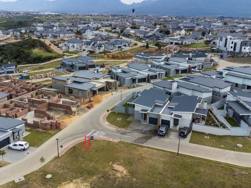 Aerial view of a vacant residential plot situated within a modern, established housing estate with paved street access and surrounding infrastructure.