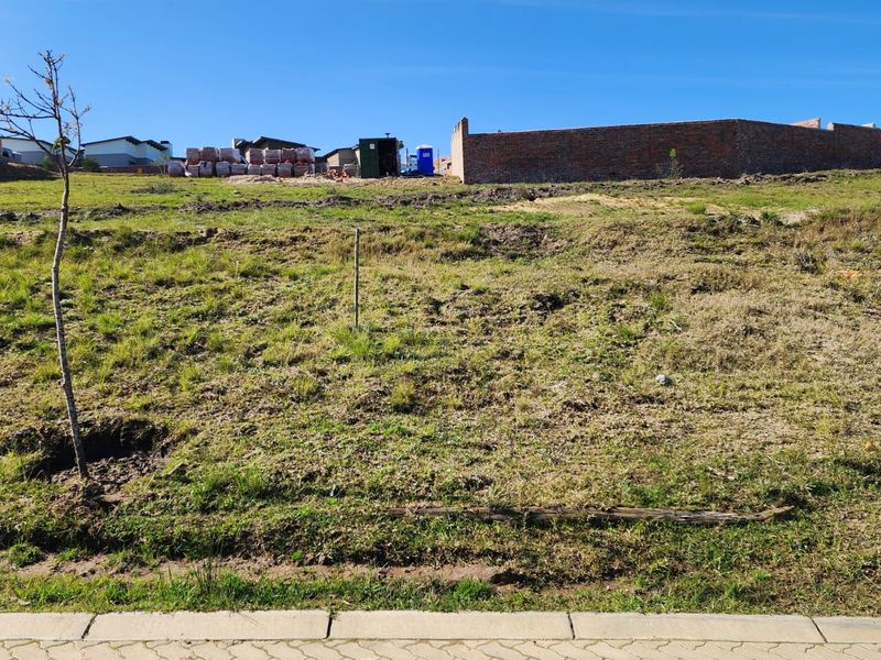 A vacant residential plot featuring a gentle slope, grass cover, and a partial brick boundary wall at the rear.