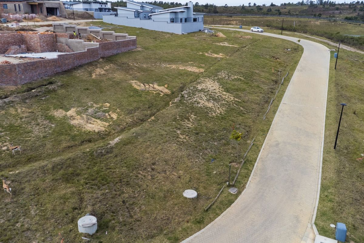Aerial view of a vacant residential plot featuring a paved access road, utility manhole covers, and surrounding estate development.
