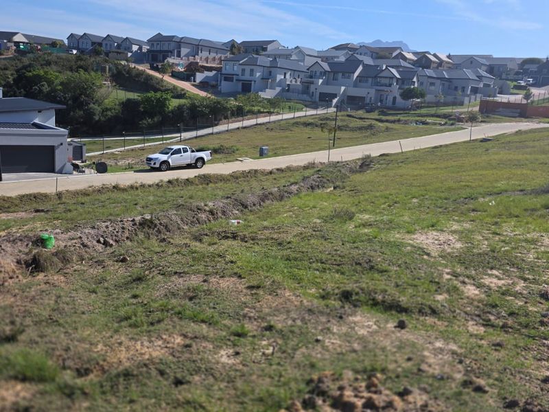 An elevated view of a vacant residential plot situated within a developed estate, featuring surrounding infrastructure and established neighboring homes.