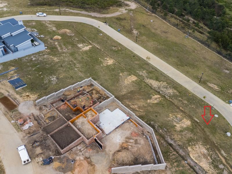 Aerial view of a residential property under construction, showing the foundation, brickwork, and concrete slab on a vacant plot.